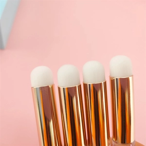 Close-up of four mini lip brushes with round white bristles and gold handles on pink