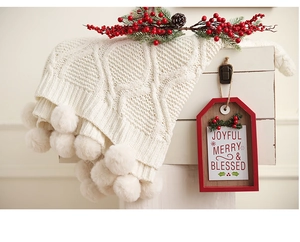 Detail of cable knit cream blanket with large soft pompoms for festive home decor