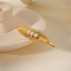 Detail shot of a golden sunburst hair clip with three white pearls on a ceramic dish