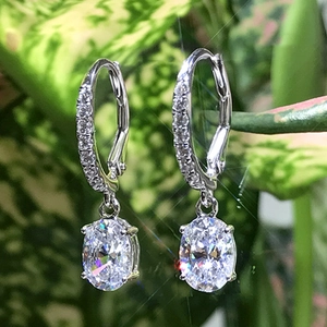 Macro di orecchini a goccia in argento con zirconi ovali e sfondo di foglie verdi