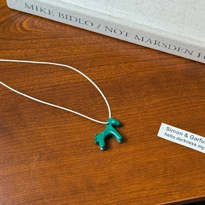 Close-up of green pony pendant on wood background with artistic book and card