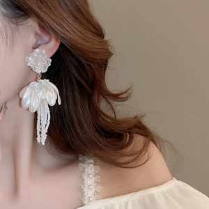 Detail of white flower tassel earrings with layered petals and beaded fringes on model