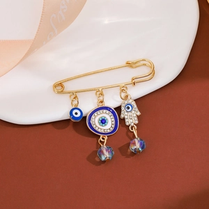 Macro detail of gold evil eye and Hamsa hand brooch charms with sparkling blue rhinestones