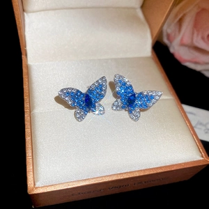 Détail de boucles d'oreilles papillon avec cristaux bleus et blancs dans un écrin de luxe