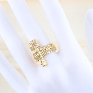Detailed view of a gold safety pin ring featuring shimmering zircon stones on a hand model