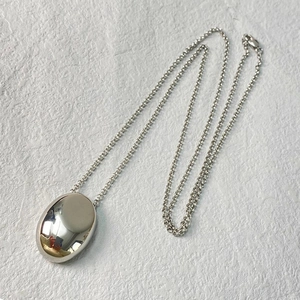 Sleek silver teardrop long sweater necklace with high-polished oval pendant on white texture