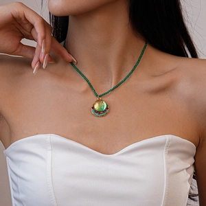 Close-up of green beaded necklace with colorful round gold-edged pendant on model