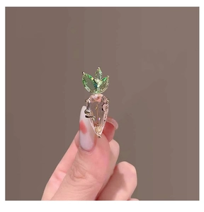 Close-up of pink crystal carrot brooch with green leaves on gold metal setting