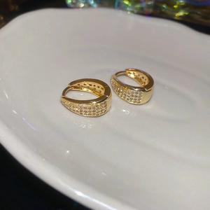 Macro shot of gold-plated U-shaped zircon hoop earrings on a white ceramic plate