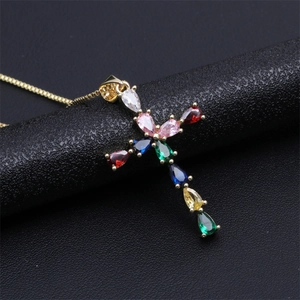 Detail view of golden cross pendant with vibrant multi-colored gemstones on black leather