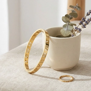 Détail d'un bracelet ajouré à chiffres romains et bague assortie contre une tasse