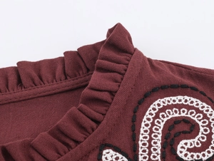 Dettaglio del colletto a balze e ricamo nero-bianco su camicia di lino rosso scuro