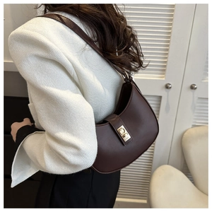 Detail of dark brown leather crescent bag with golden twist lock on a white tweed jacket