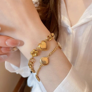 Detail of layered gold bracelets with heart, star, and shell charms on wrist