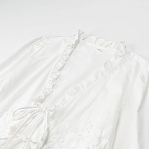 Detail of white embroidery blouse with ruffled edges and tie-front drawstring closure