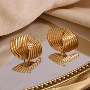 Macro shot of gold-plated fan-shaped striped earrings reflecting on a mirror surface