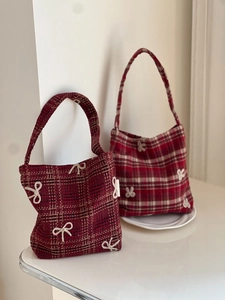 Detail of red plaid wool handbags with embroidered white bows in a minimalist indoor setting