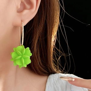 Primo piano di orecchini a fiore verde neon in acrilico con diamanti indossati da una modella