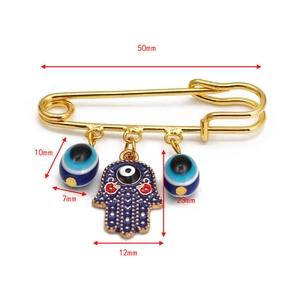 Detailed view of Hamsa Hand and Evil Eye charms on a gold-tone safety pin brooch