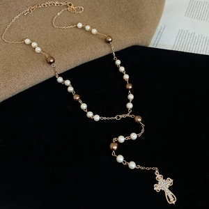 Detailed close-up of a vintage cross pendant with crystals on a pearl Y-necklace chain