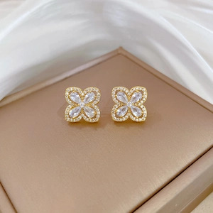 Detail of gold clover stud earrings with pavé zircons on silk background