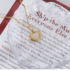 Macro view of gold heart pendant necklace with white mother of pearl inlay on ice texture