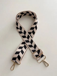 Close-up of beige and black geometric patterned canvas bag strap with gold metal buckles