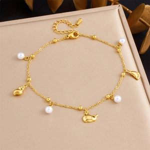 Close-up of gold stainless steel anklet with shell, whale, and pearl charms on box