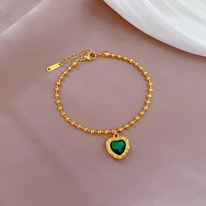 Macro detail of gold beaded bracelet with green heart charm on silk fabric background