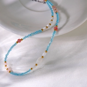 Detail of beaded necklace with light blue stone, freshwater pearl, and gold accents on satin