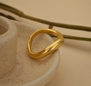 Detailed close-up of a wavy gold vermeil ring on a beige ceramic base with artistic branches