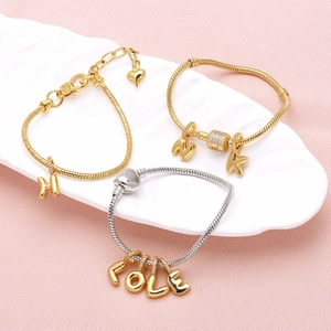 Gold and silver snake chain bracelets with letter pendants on a white leaf tray