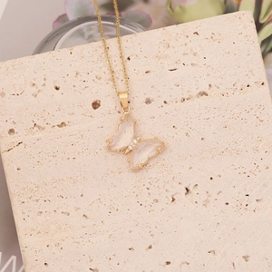 Détail du collier papillon doré avec ailes en cristal sur une surface en pierre beige
