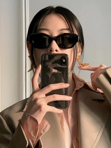 Close-up of black cat-eye sunglasses and gold high-heel earrings with a camel blazer