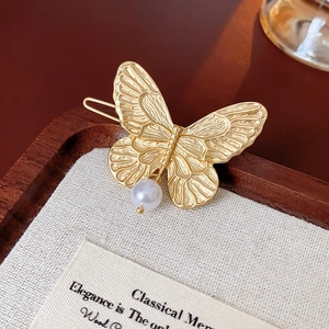 Close-up of golden butterfly hair clip with white pearl detail on textured fabric