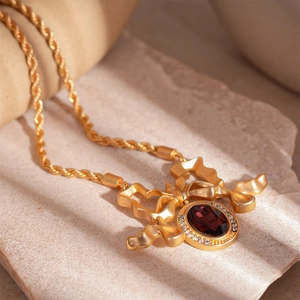Detail of vintage gold bow pendant with deep red oval gemstone and tiny diamonds