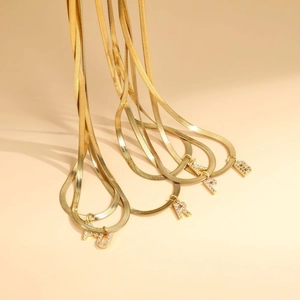 Close-up of gold snake chain necklaces with pavé zircon initial letter pendants