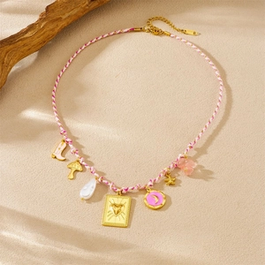 Pink woven necklace with gold charms like boots and mushrooms on a sandy surface