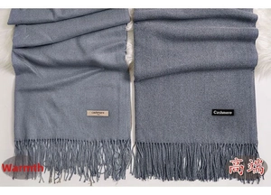 Detailed view of grey-blue cashmere scarf texture with delicate fringe and brand label