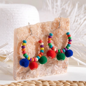 Macro detail of colorful beaded hoop earrings with plush pom-poms on a stone texture