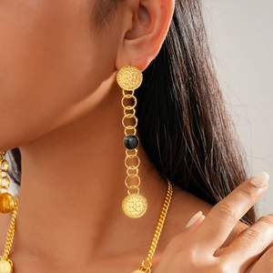 Close-up of golden tassel earrings with black beads and coin pendant on a female model