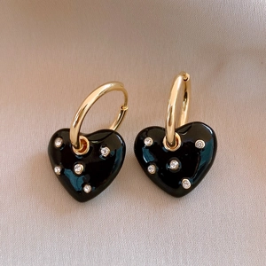 Close-up of vintage golden heart earrings with black enamel and sparkling zircon detail