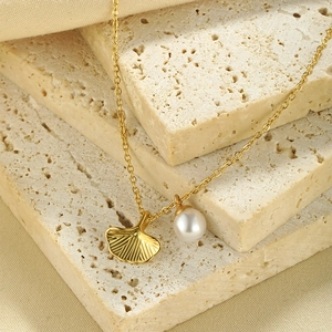 Detailed macro view of ginkgo leaf pendant with pearl on textured stone block