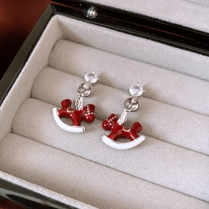 Detailed macro view of silver horse earrings with red enamel and zircon on grey velvet