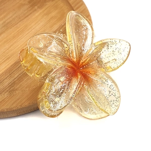 Detailed view of yellow frangipani flower hair claw clip with golden glitter details