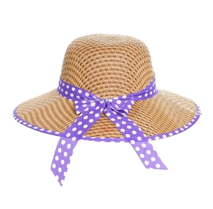 Detail of a brown woven straw sun hat featuring a purple polka dot ribbon bow decoration