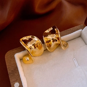 Detail view of irregular gold wavy square stud earrings resting in a premium jewelry box