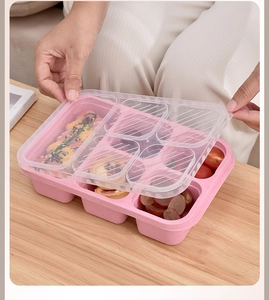 Pink wheat straw lunch box with five compartments and a clear lid on a wooden table