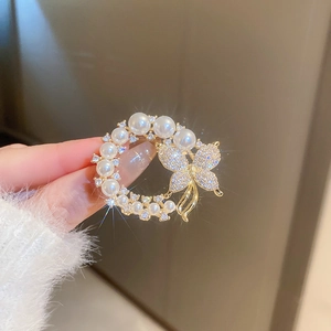 Détail d'une broche fleur dorée avec perles, zircons et papillon tenue à la main