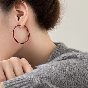 Close-up of a large red twisted hoop earring with glossy finish on a female model
